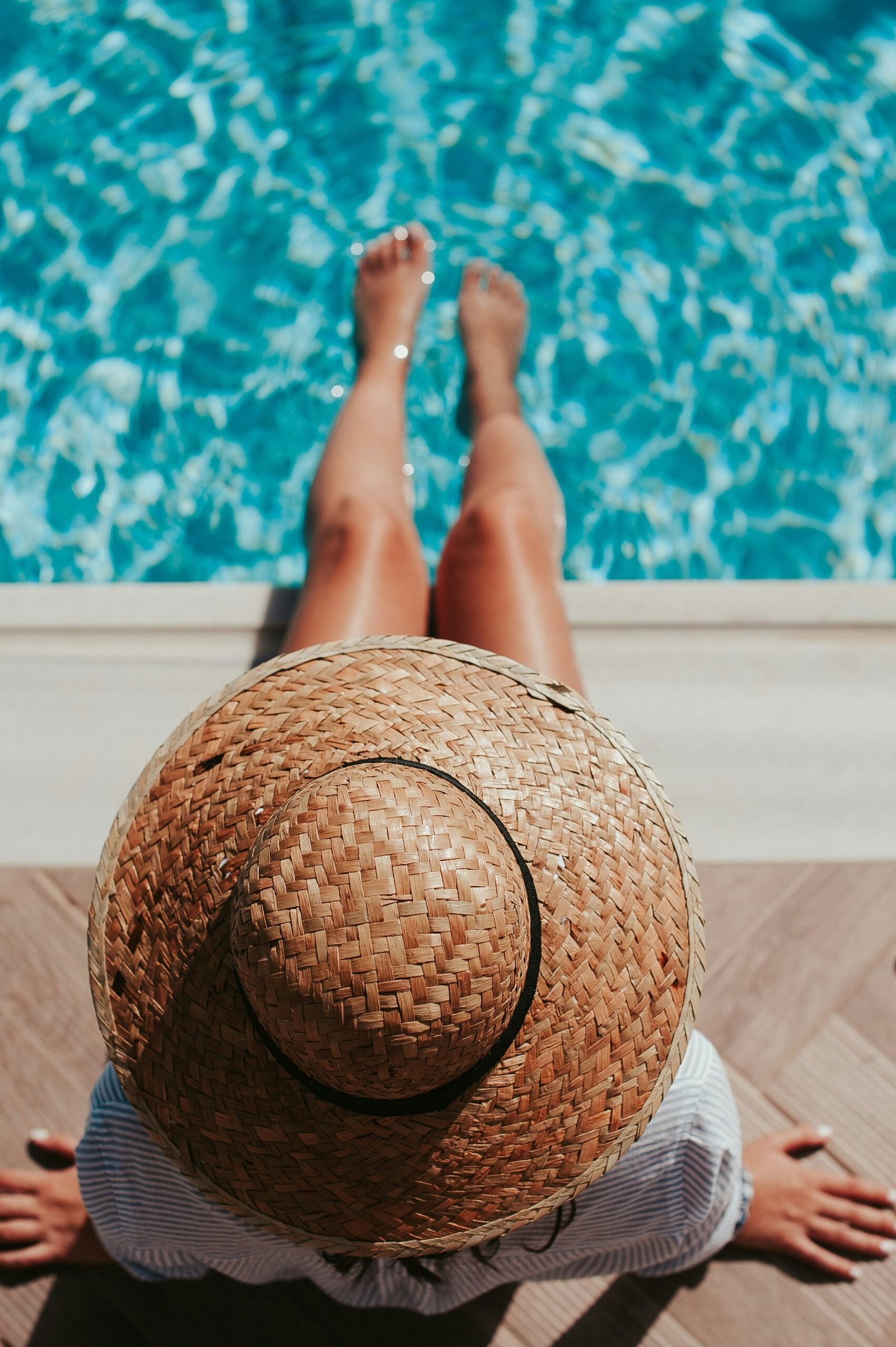 woman sitting on poolside setting both of her feet on pool